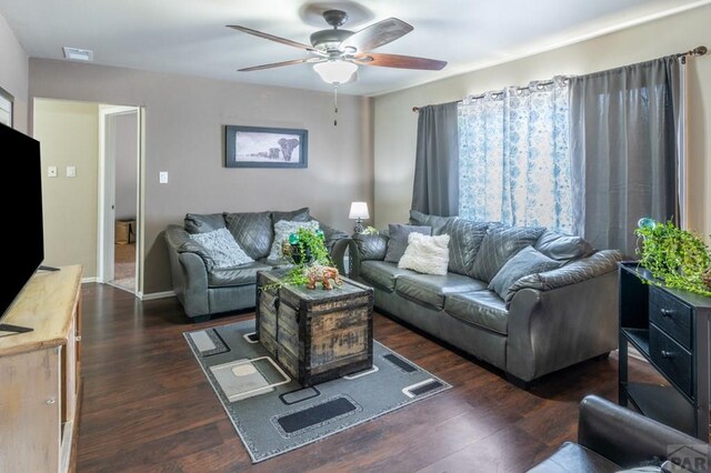 living room with dark wood-type flooring, visible vents, ceiling fan, and baseboards