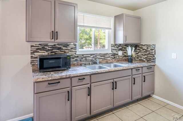 kitchen with black microwave, tasteful backsplash, a sink, and gray cabinetry