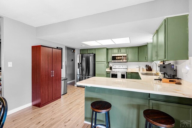 kitchen with light countertops, appliances with stainless steel finishes, a sink, a peninsula, and a kitchen breakfast bar