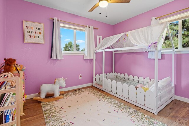 bedroom featuring multiple windows, wood finished floors, a ceiling fan, and baseboards