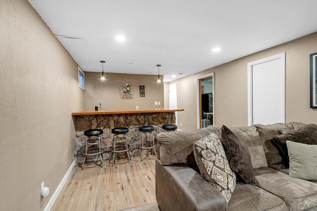 interior space featuring baseboards, light wood-style flooring, decorative light fixtures, wet bar, and recessed lighting