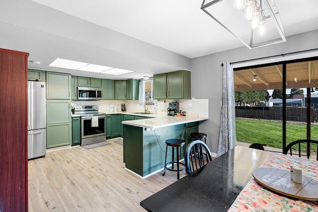 kitchen with appliances with stainless steel finishes, light countertops, a peninsula, and green cabinets