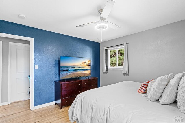 bedroom featuring light wood-style floors, baseboards, a ceiling fan, and a textured wall