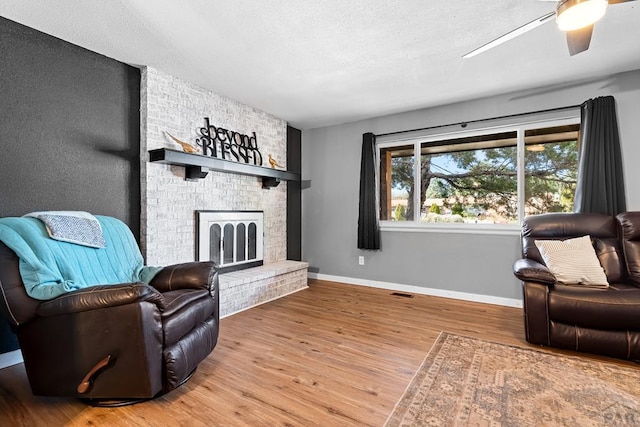 living area with a ceiling fan, a brick fireplace, a textured ceiling, wood finished floors, and baseboards