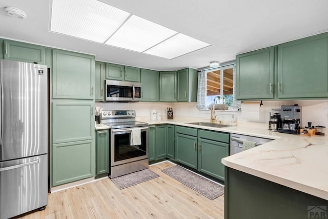 kitchen featuring appliances with stainless steel finishes, a sink, light stone countertops, and green cabinetry