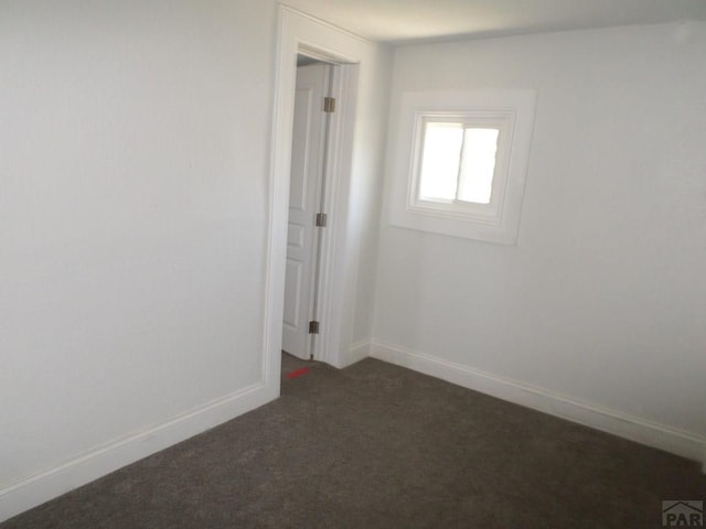 empty room featuring baseboards and dark carpet