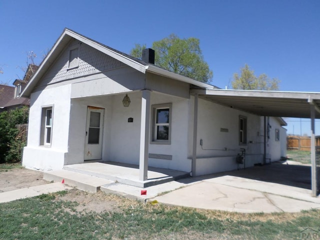 view of front of property with covered porch, a chimney, fence, an attached carport, and stucco siding