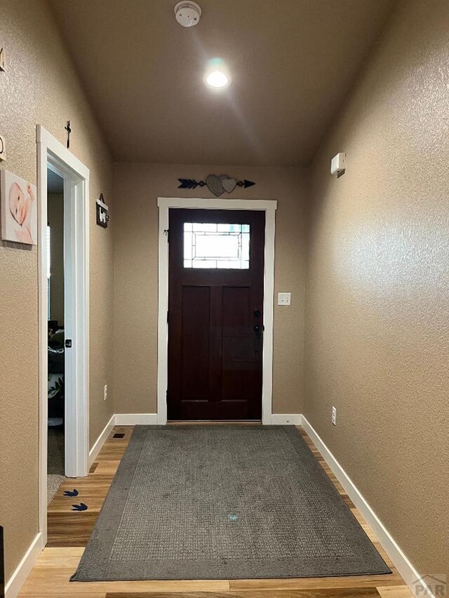 foyer entrance featuring a textured wall, baseboards, and wood finished floors