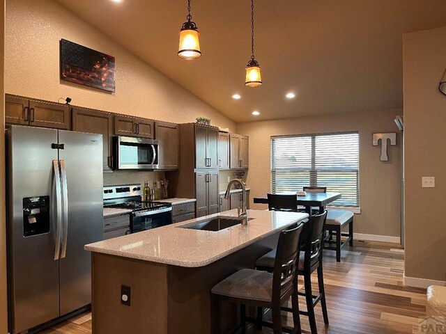 kitchen featuring decorative light fixtures, stainless steel appliances, a sink, dark brown cabinets, and a center island with sink