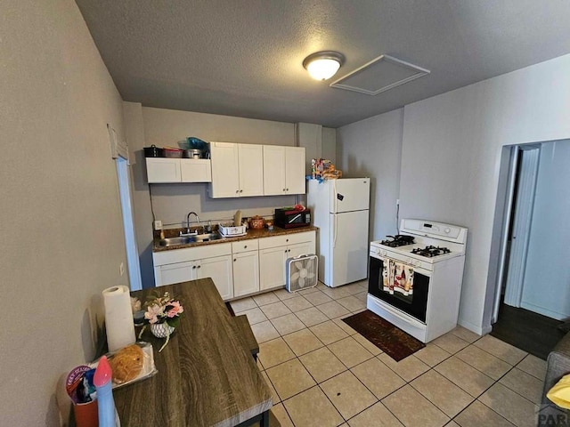 kitchen featuring white appliances, light tile patterned floors, white cabinets, dark countertops, and a sink