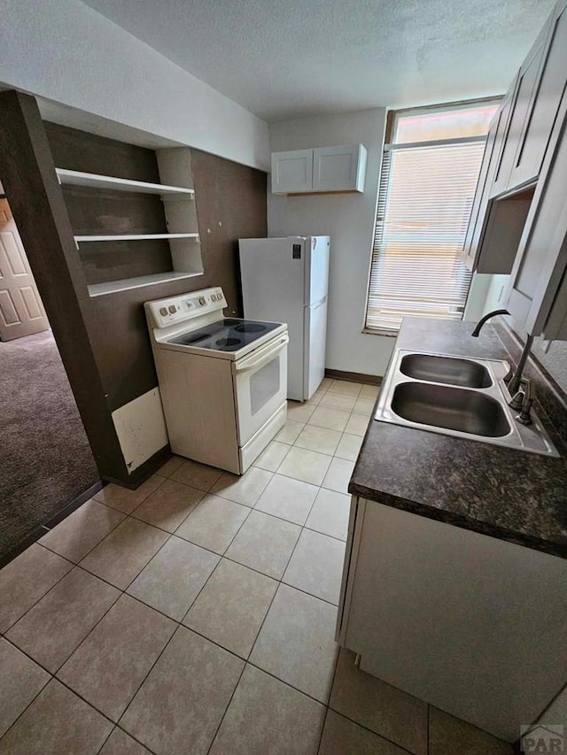 kitchen with a textured ceiling, light tile patterned floors, white appliances, a sink, and white cabinetry