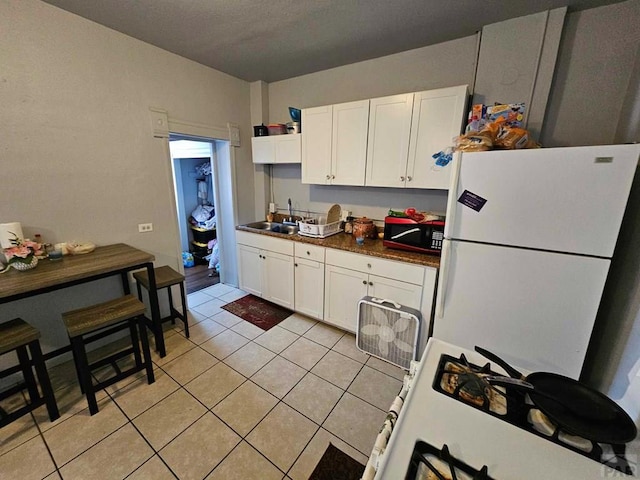 kitchen featuring dark countertops, a sink, freestanding refrigerator, and white cabinets