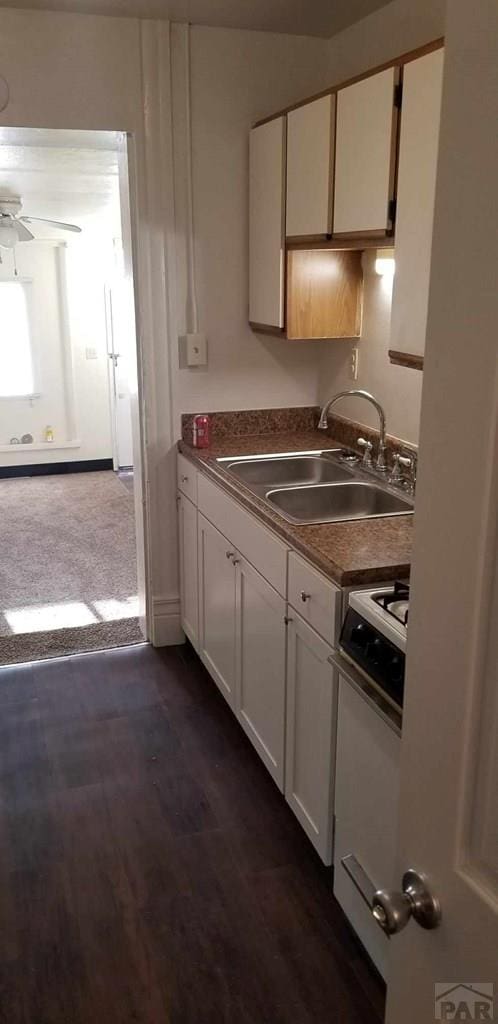 kitchen featuring gas range gas stove, dark countertops, a sink, and white cabinets