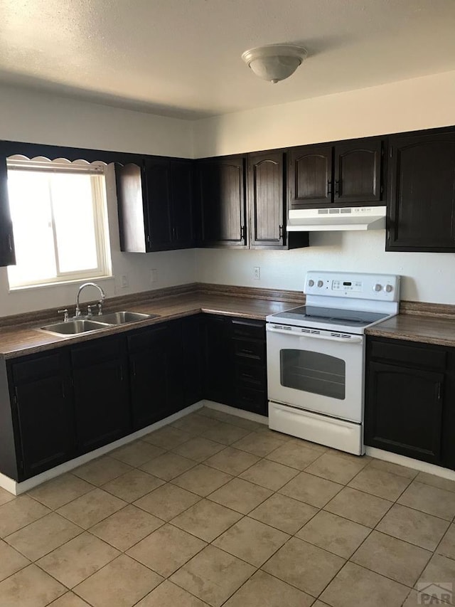 629 E Clarion Dr, Pueblo, CO 81007 - kitchen with white electric stove, under cabinet range hood, light tile patterned flooring, dark cabinets, and dark countertops