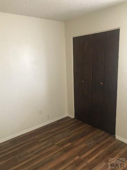 629 E Clarion Dr, Pueblo, CO 81007 - unfurnished bedroom with dark wood-style floors, a closet, and a textured ceiling