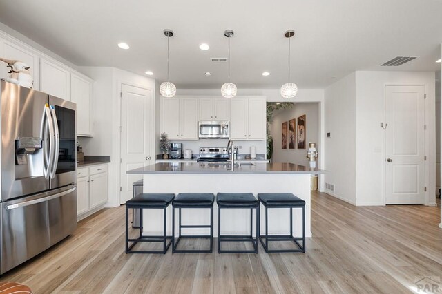 kitchen with hanging light fixtures, white cabinetry, a center island with sink, and appliances with stainless steel finishes