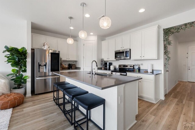 kitchen with decorative light fixtures, white cabinetry, appliances with stainless steel finishes, dark countertops, and a center island with sink