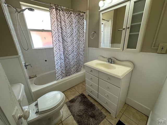 full bath featuring tile patterned flooring, a wainscoted wall, shower / tub combo with curtain, and toilet