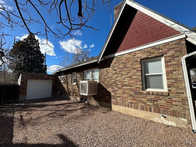 view of home's exterior featuring brick siding, central AC, a garage, an outdoor structure, and driveway