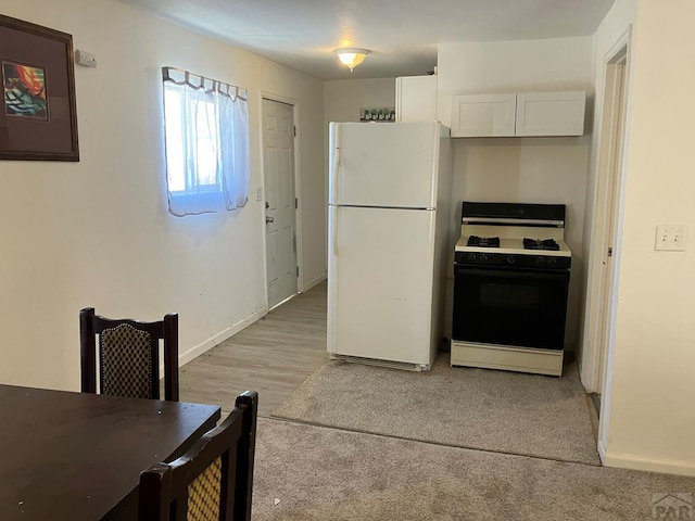 kitchen featuring freestanding refrigerator, white cabinetry, baseboards, and gas range