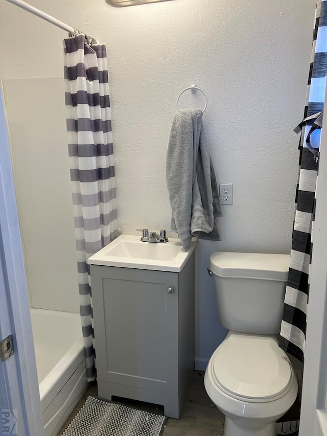 full bathroom featuring shower / bath combo, a textured wall, vanity, and toilet