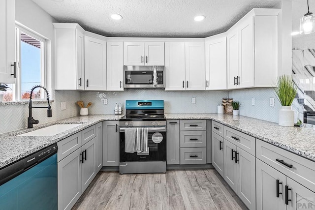 kitchen featuring appliances with stainless steel finishes, a sink, light wood-style flooring, and gray cabinetry