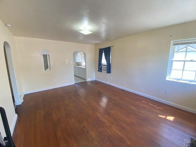 unfurnished room featuring dark wood-style floors, baseboards, and arched walkways