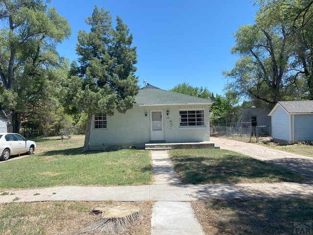 bungalow-style home featuring stucco siding, roof with shingles, fence, and a front yard