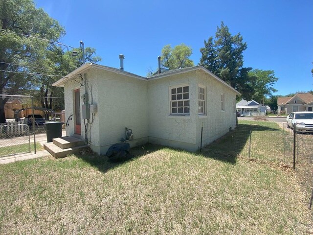 view of side of property featuring fence, a lawn, and stucco siding