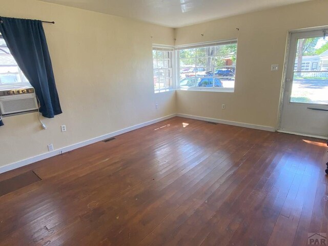 unfurnished room with baseboards, visible vents, dark wood finished floors, and cooling unit