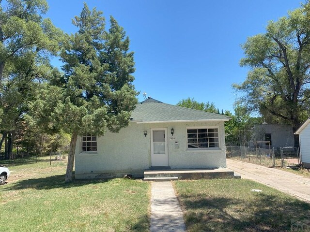 bungalow-style home with roof with shingles, fence, a front lawn, and stucco siding