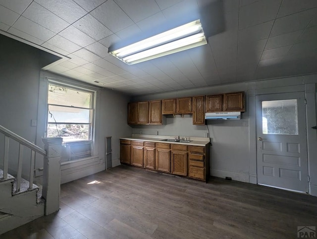 kitchen with dark wood-style floors, brown cabinets, light countertops, a sink, and under cabinet range hood