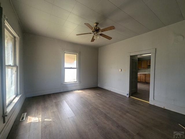 spare room with dark wood-type flooring, a ceiling fan, visible vents, and baseboards