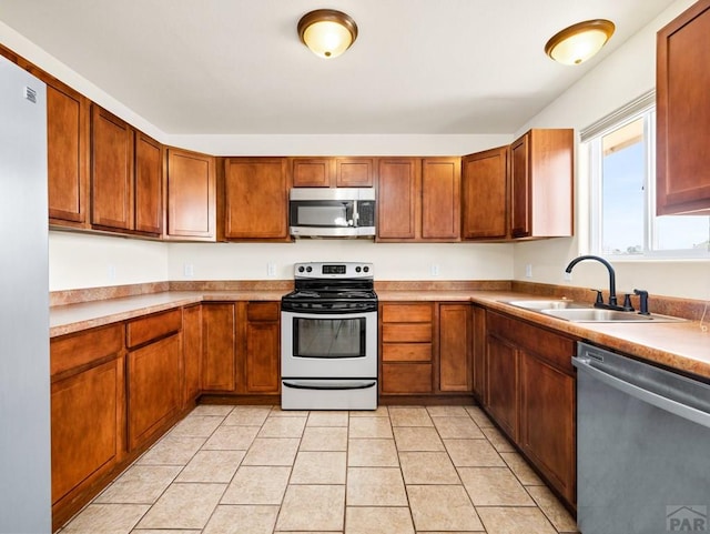 kitchen featuring a sink, light tile patterned flooring, brown cabinets, light countertops, and appliances with stainless steel finishes