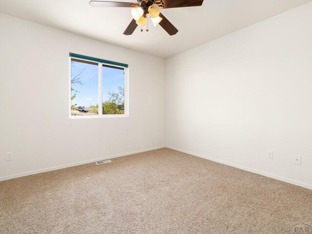 carpeted spare room with baseboards, a ceiling fan, and visible vents