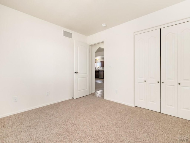 unfurnished bedroom featuring light carpet, baseboards, visible vents, and a closet