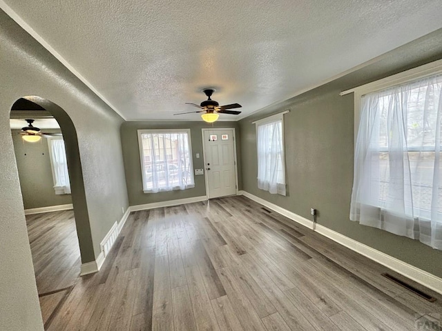 entryway featuring arched walkways, visible vents, a textured wall, light wood-style floors, and baseboards