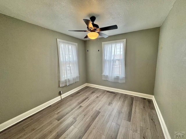 spare room with light wood finished floors, a ceiling fan, visible vents, and baseboards