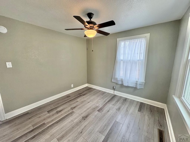 empty room featuring baseboards, visible vents, a textured ceiling, and light wood finished floors