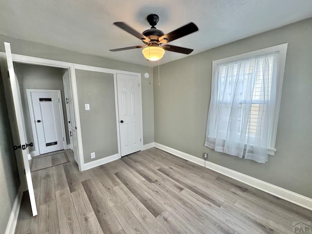 unfurnished bedroom featuring a ceiling fan, a closet, light wood-style flooring, and baseboards