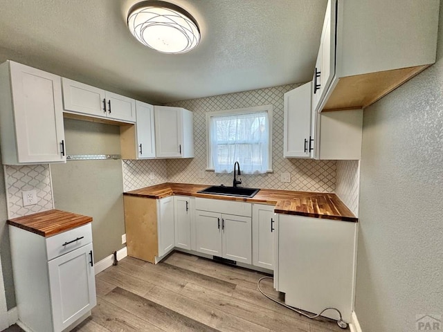 kitchen featuring backsplash, light wood-style flooring, white cabinetry, a sink, and butcher block countertops