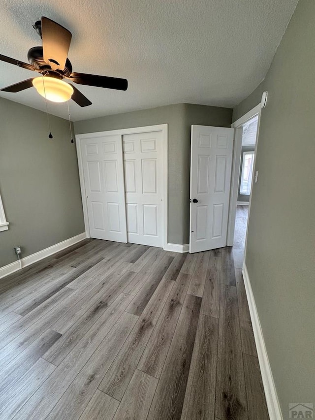 unfurnished bedroom with ceiling fan, a textured ceiling, baseboards, light wood-style floors, and a closet