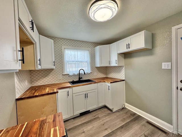 kitchen with butcher block countertops, visible vents, a sink, and white cabinetry