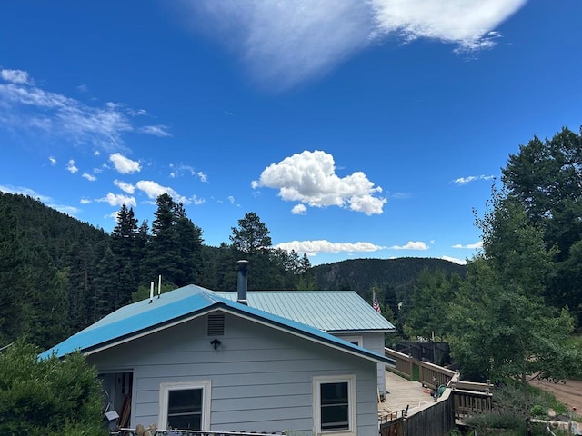 view of property exterior with metal roof, a deck with mountain view, and a wooded view