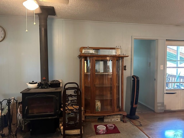 living area with a wood stove, a textured ceiling, and wood finished floors