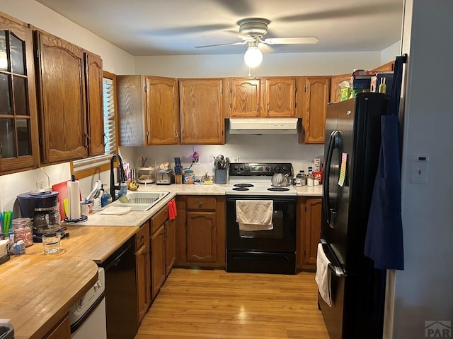 kitchen with brown cabinetry, light wood-style floors, under cabinet range hood, black appliances, and a sink