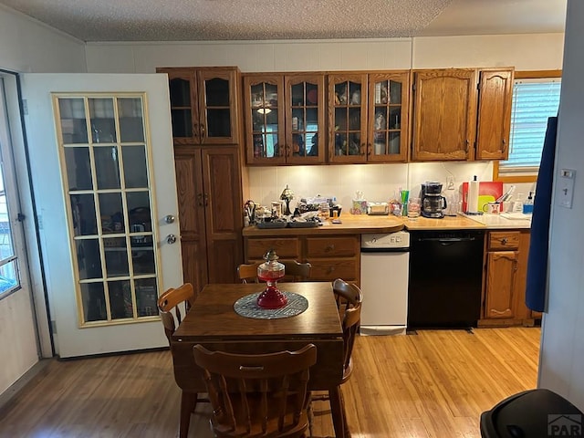 kitchen with black dishwasher, glass insert cabinets, light countertops, and light wood-style flooring