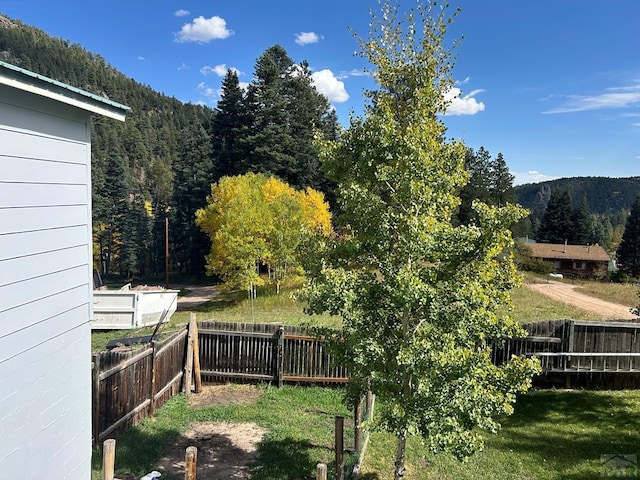 view of yard featuring a wooded view, a fenced backyard, and a mountain view