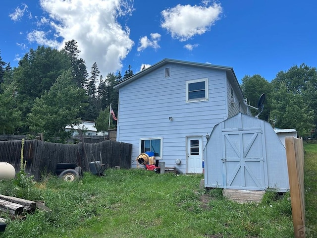 rear view of property with fence, an outdoor structure, and a shed