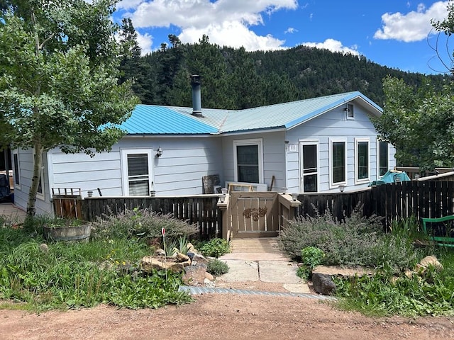 rear view of house with metal roof, a forest view, and fence